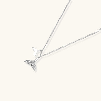 Delicate white gold plated whale tail pendant with pavé crystals on silver chain against cream background.