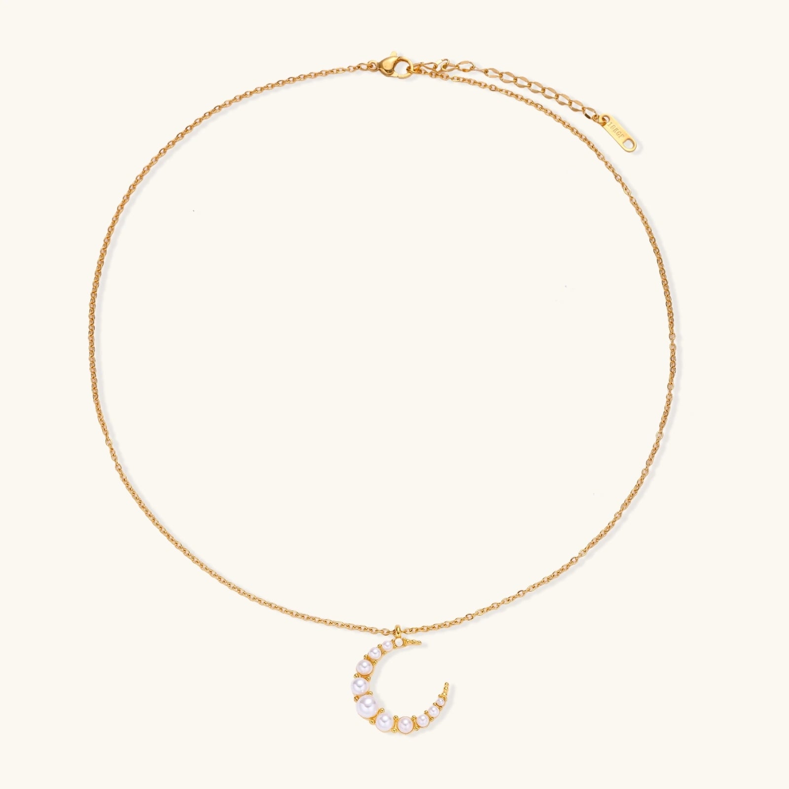 Gold crescent moon pendant with graduated white pearls on delicate chain against cream background
