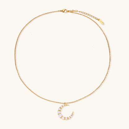 Gold crescent moon pendant with graduated white pearls on delicate chain against cream background