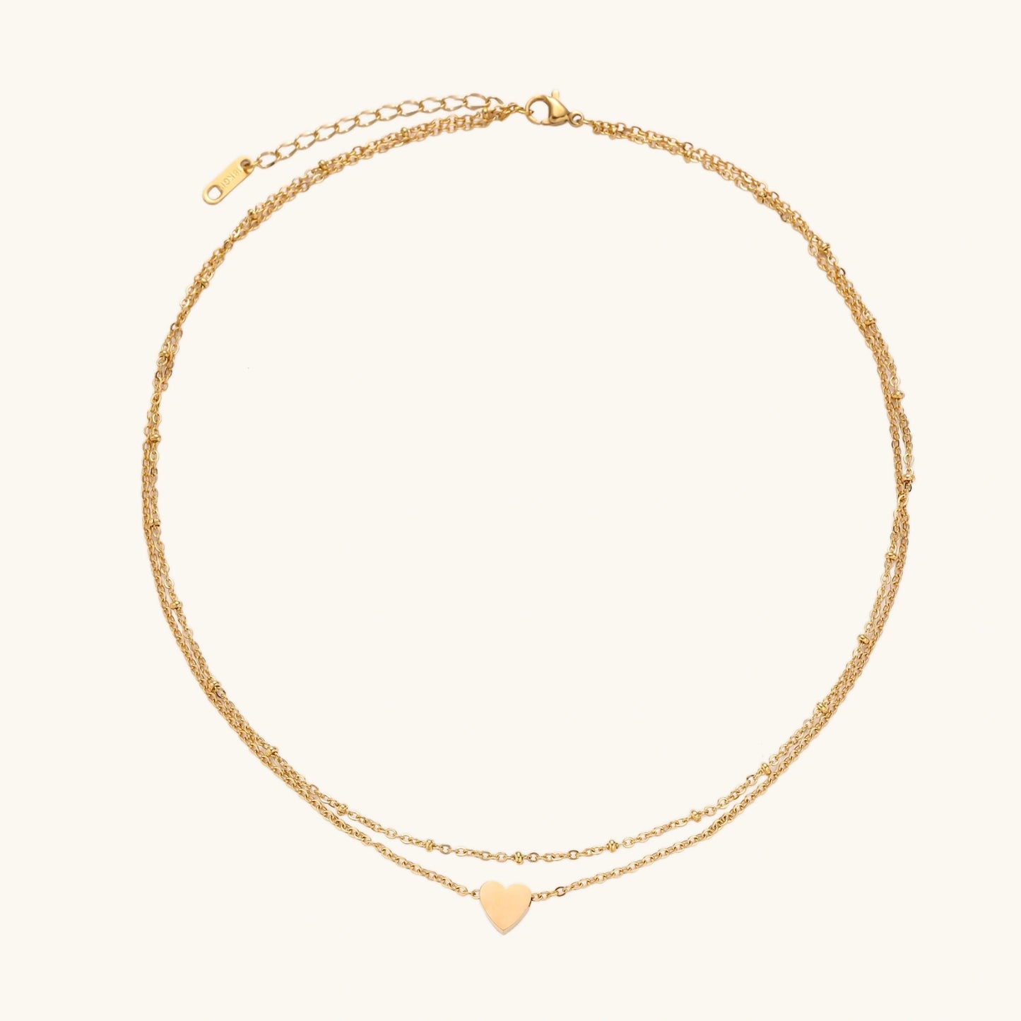 Delicate double-chain gold necklace with tiny heart pendant on cream background