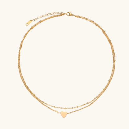 Delicate double-chain gold necklace with tiny heart pendant on cream background