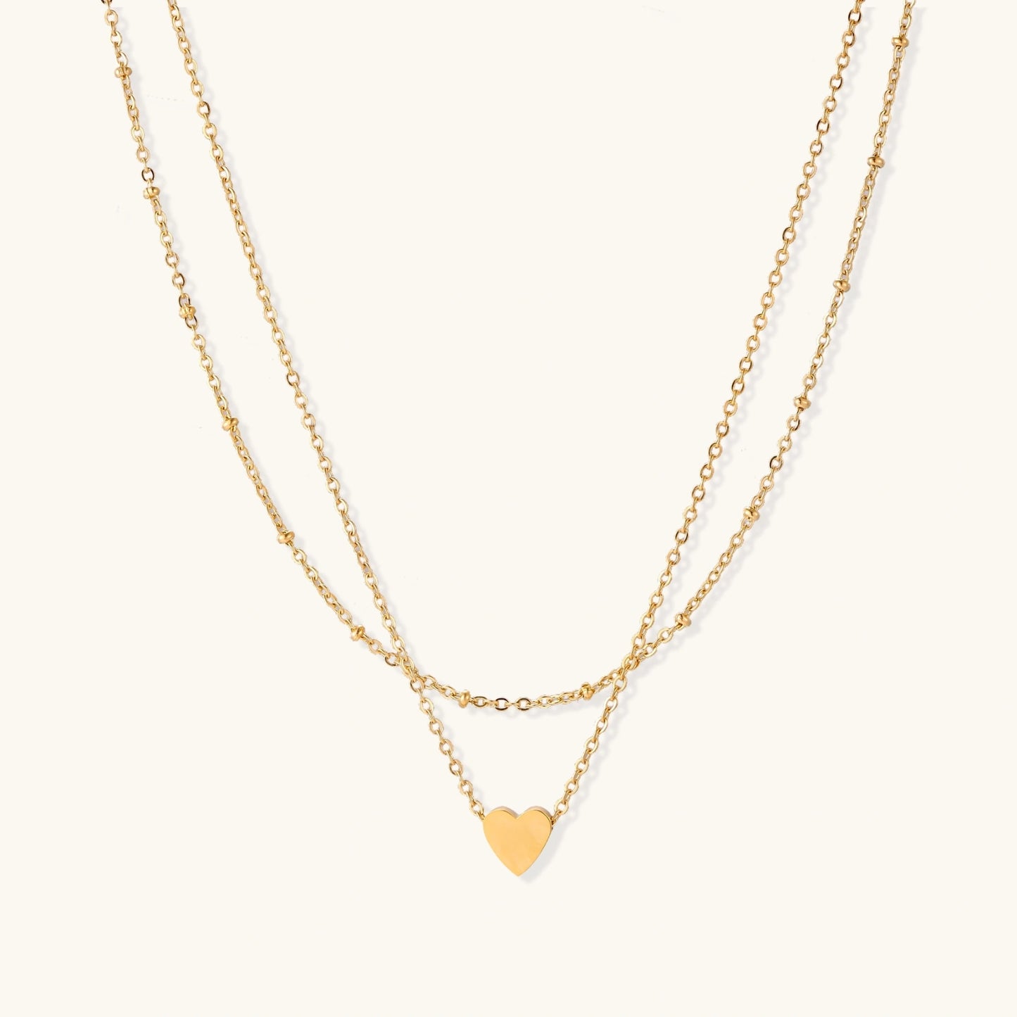 Delicate double-chain gold necklace with tiny heart pendant on cream background