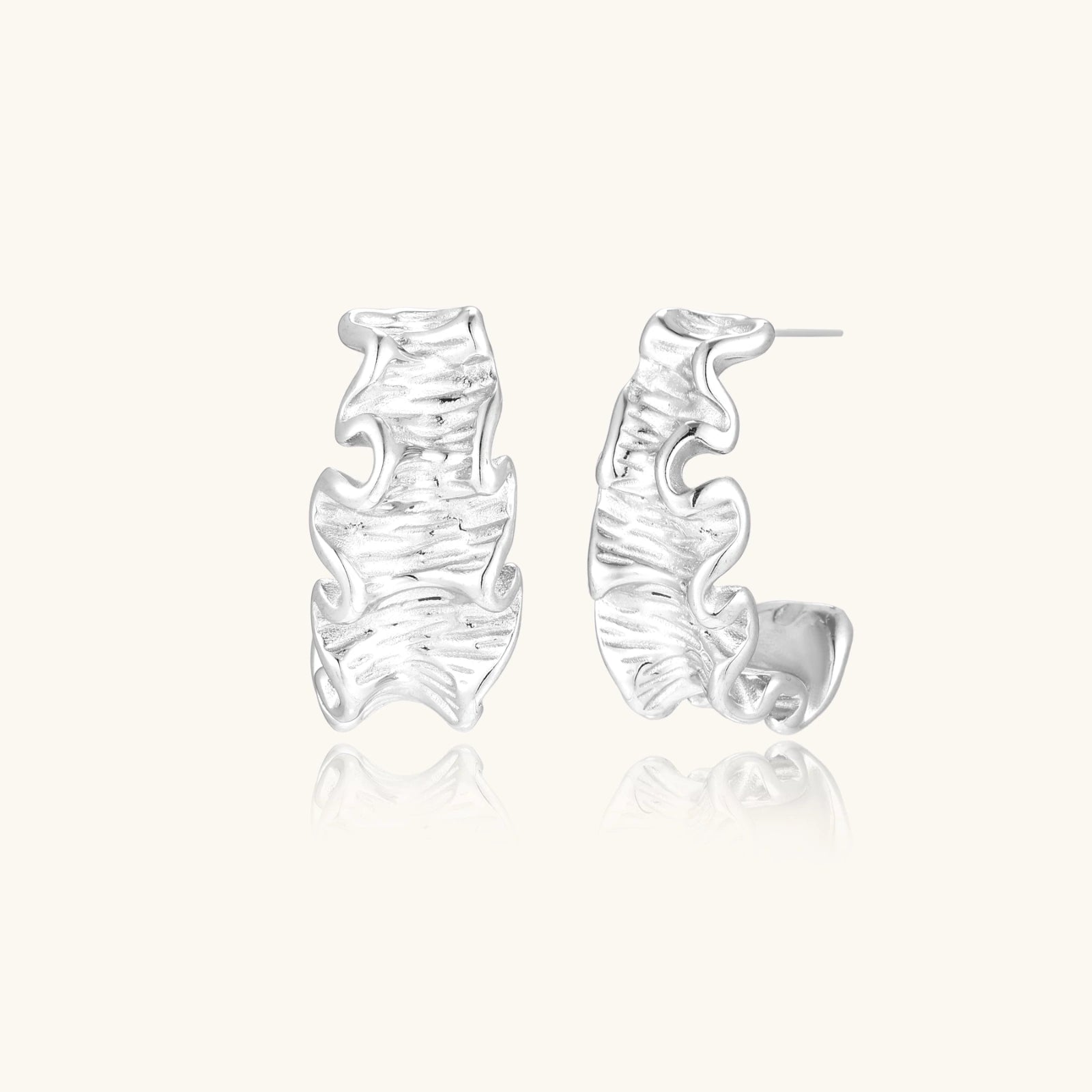 White gold plated sculptural hoop earrings with organic wavy edges and reflective metallic finish on cream background