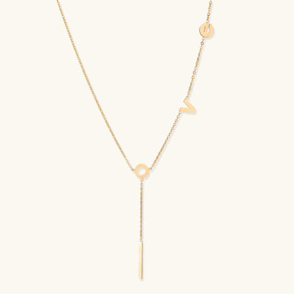 Gold Y-shaped necklace with L-O-V-E letter charms and vertical bar pendant on delicate chain against cream background