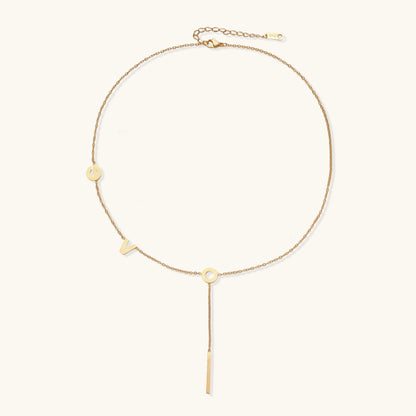 Gold Y-shaped necklace with L-O-V-E letter charms and vertical bar pendant on delicate chain against cream background