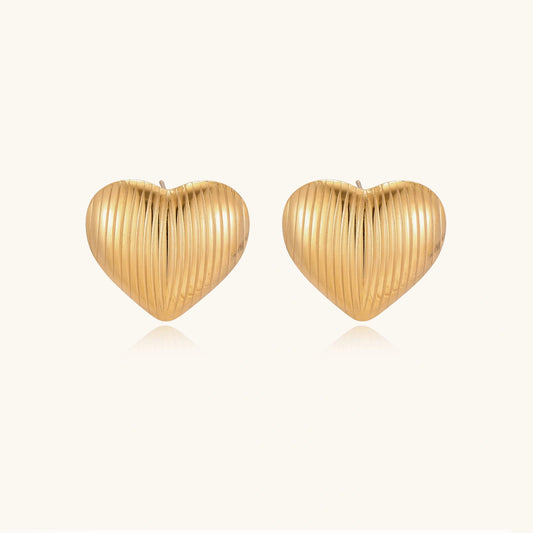 Gold heart-shaped stud earrings with parallel ridged texture on cream background