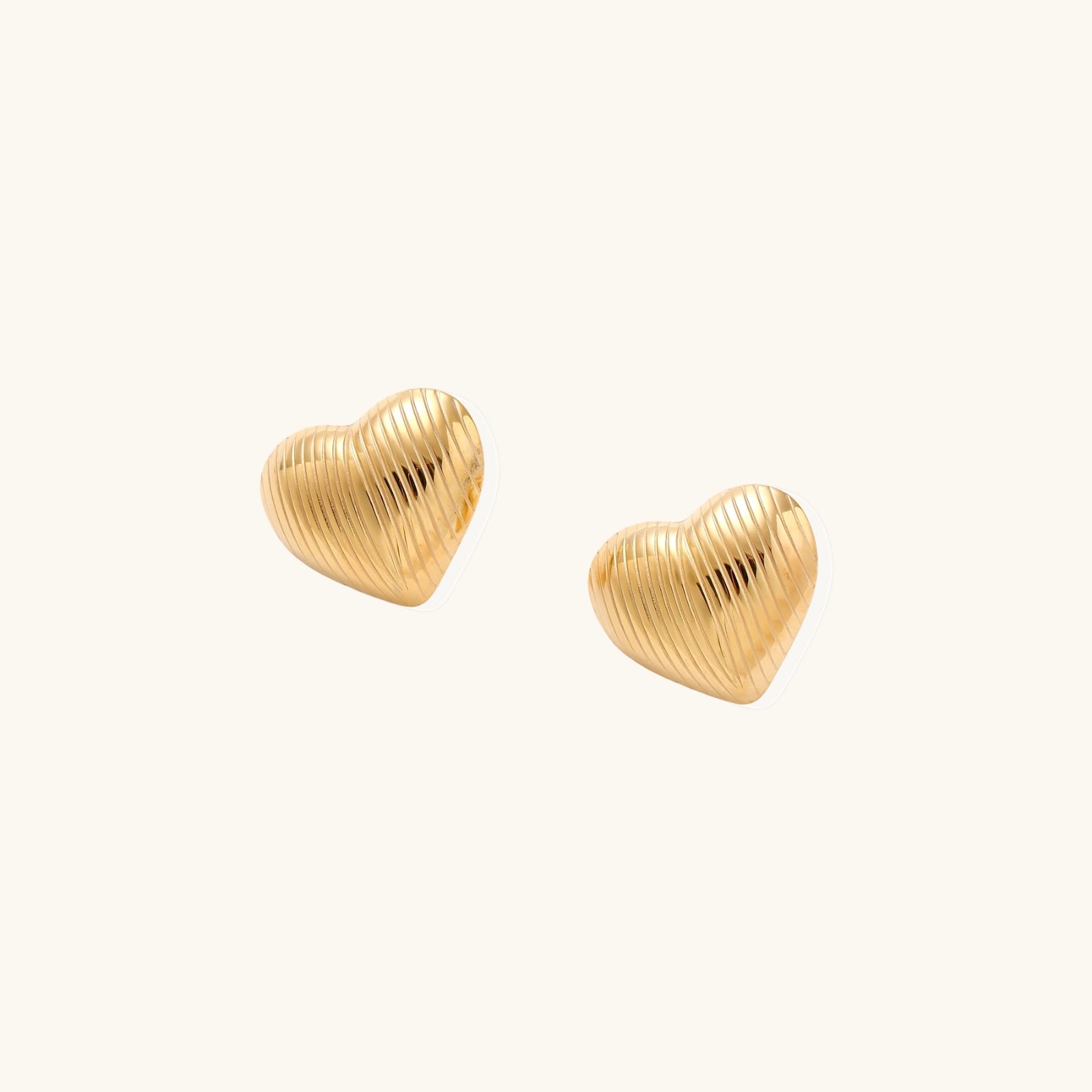 Gold heart-shaped stud earrings with parallel ridged texture on cream background