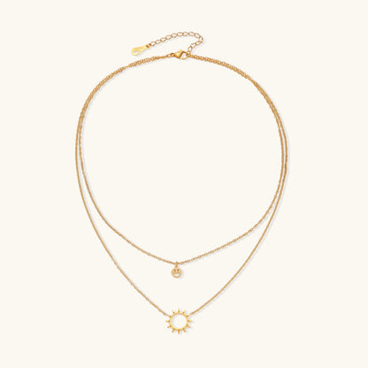 Gold layered necklace set with sunburst and smiley face pendants on delicate chains against white background.