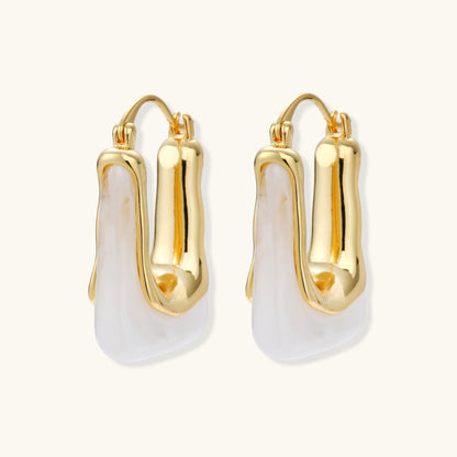 Sculptural gold-plated hoop earrings with flowing curved design and lever-back closure on cream background.